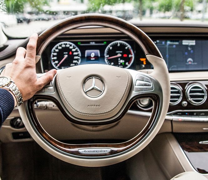 Une main d'homme est posée sur le volant d'une voiture de marque Mercedes